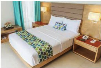 Chambre A : lit double avec tête de lit en bois et couvre-lit à motifs colorés.