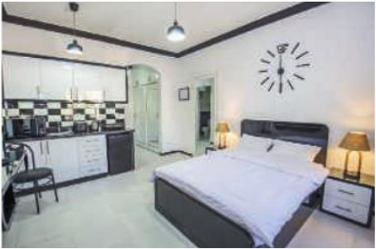 Chambre C : studio avec lit double, coin cuisine et pendule murale.
